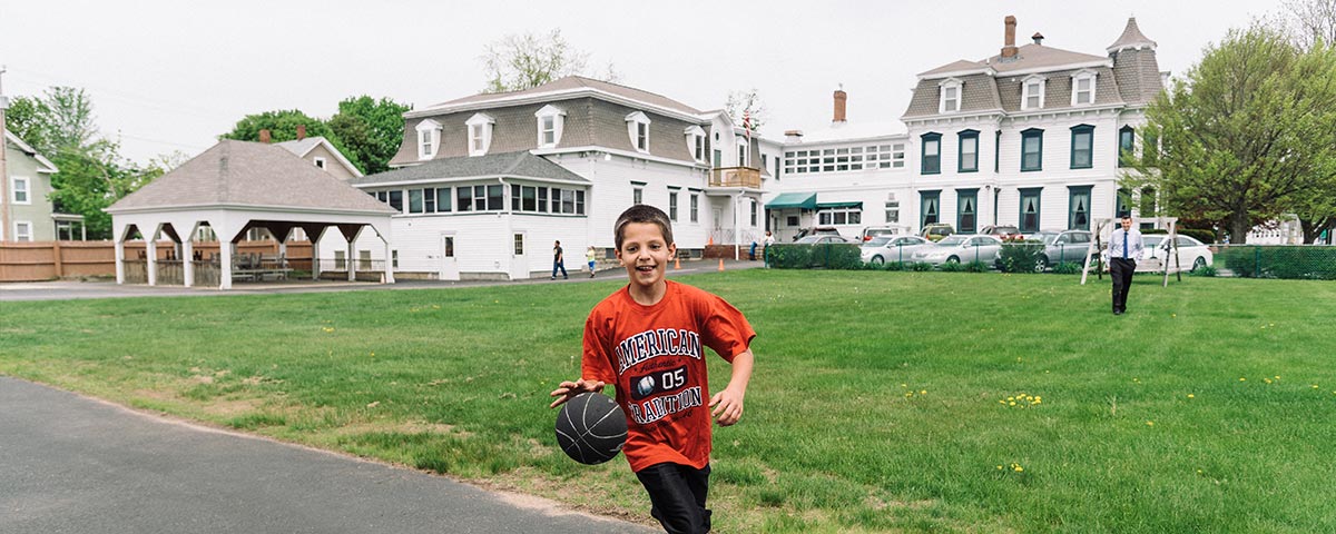 A child dribbles a basketball in the playground at the St. Charles School in Rochester, NH. St. Charles School program requirements image.
